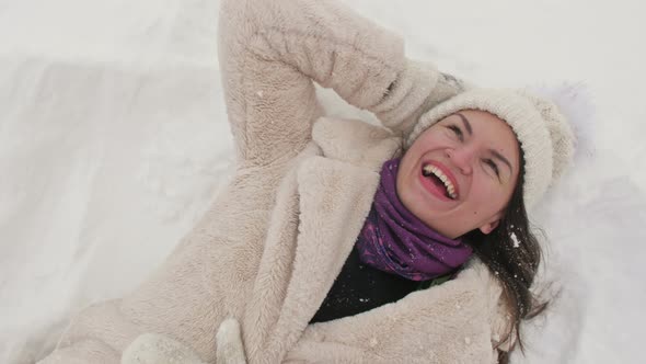 Young Woman Lies in the Snow and Laughs Cheerfully