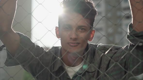 Close-up Portrait of Young African American Man in Sunlight Behind Mesh Fence. Happy Confident Guy