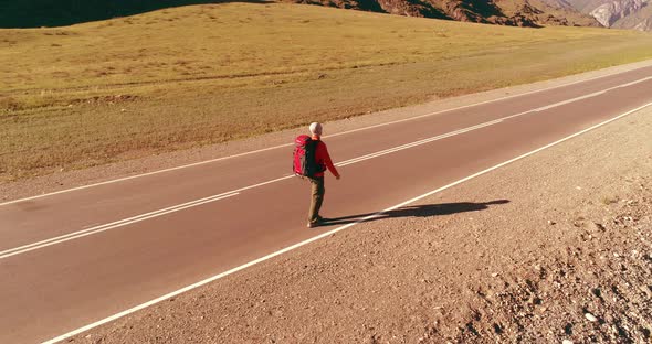 Flight Over Hitchhiker Tourist Walking on Asphalt Road. Huge Rural Valley at Summer Day. Backpack alt