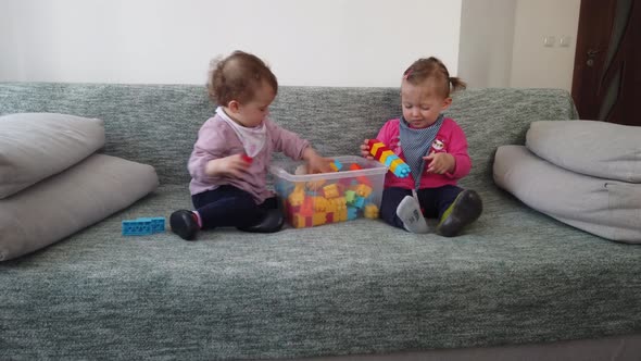 Two sisters girls, playing with toys on the sofa at home alt
