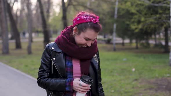 Beautiful Young Stylish Woman Walks in the Park with a Cup of Coffee. Modern Girl in a Leather