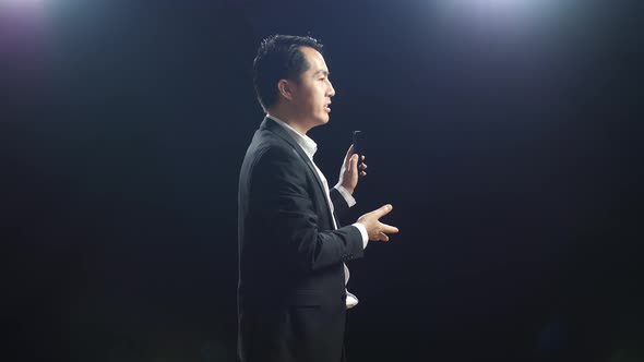 Side View Of Asian Speaker Man In Business Suit Holding And Pointing Smartphone While Speaking