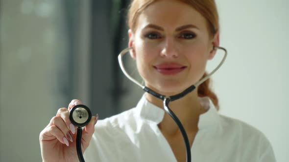 Close-up of Woman Doctor in White Coat in Clinic at Workplace Holds Stethoscope in His Hand and