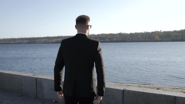 Businessman Goes To the River Along the Promenade in the City