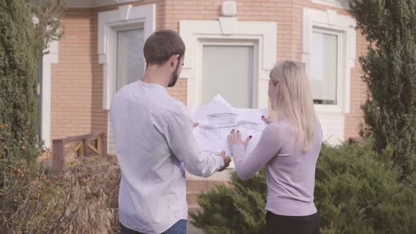 Male Caucasian Architect and His Female Assistant Examining Blueprints in Front of the House and