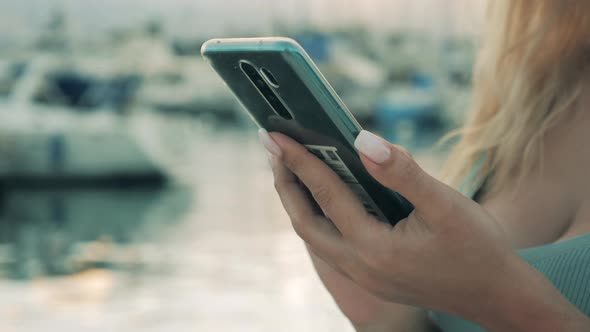 A Woman Works with Smartphone While Standing in a Port