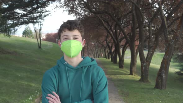 A young man in a medical protective mask on the path against the background of trees