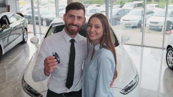 Visiting Car Dealership. Beautiful Couple Is Holding a Key of Their New Car, Looking at Camera and