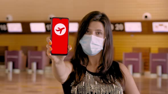 Woman, in Protective Mask, Holds Smartphone with COVID-19 Icon, Text - Trip Canceled, on Screen