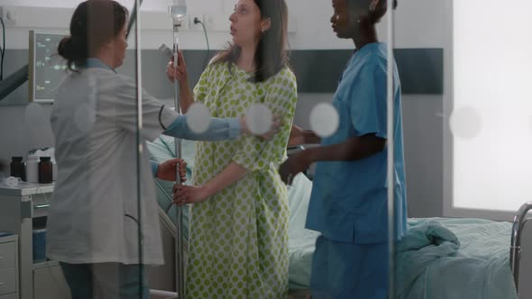 Medical Team Helping Sick Woman to Stand Up From Bed Holding Intravenous IV Fluid Drip Bag