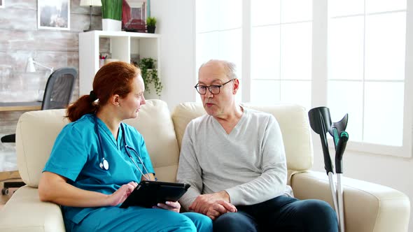 Female Caucasian Nurse Taking Notes About Elderly Man Health in Bright and Cozy Nursing Home