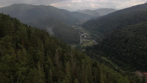 Flying over treetops looking down into valley revealing a bend in a river and clusters of homes on t