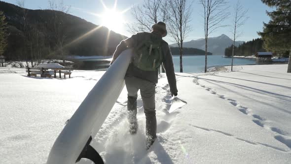 Man carrying SUP through snow to a lake