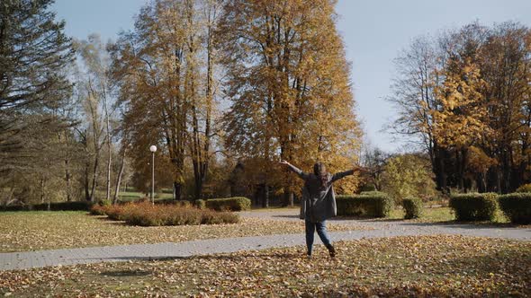 Woman in Jeans and Coat Walks in Autumn Park on Sunny Day