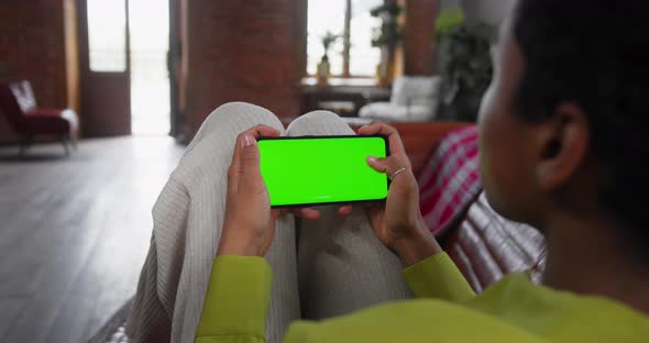 Young Woman Lying on Couch with Modern Smartphone in His Hand While Looking on Mock Up Screen
