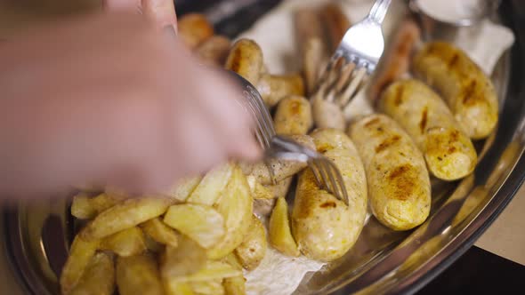 Closeup Top View Tray with Baked Grilled Fried Potato with Hands Pricking Sausages with Fork Leaving
