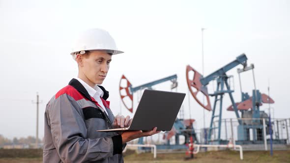 Engineer Types on a Laptop Near Oil Derrick