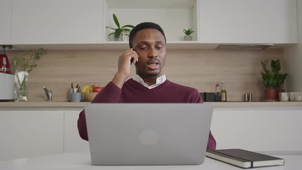 Young Adult Businessman Having a Call on His Phone in Front of His Laptop