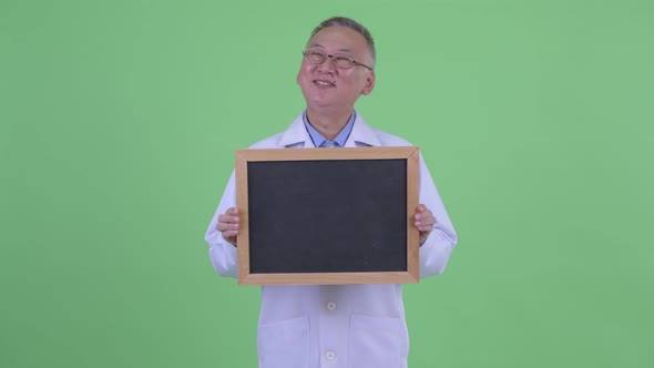 Happy Mature Japanese Man Doctor Thinking While Holding Blackboard