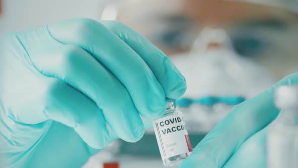 Doctor with Protective Suit and Vial with Coronavirus Vaccine