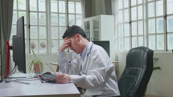 Asian Man Doctor Is Using Desktop Computer And Headache In Workplace. Medical Concept