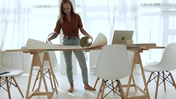 woman in office is leaning over a Desk with a design project and typing a laptop