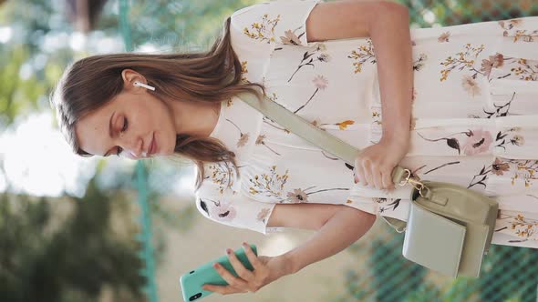 Vertical Video. Pretty Caucasian Brown Hair Girl Wearing White Flower Dress with Bag Cross Her