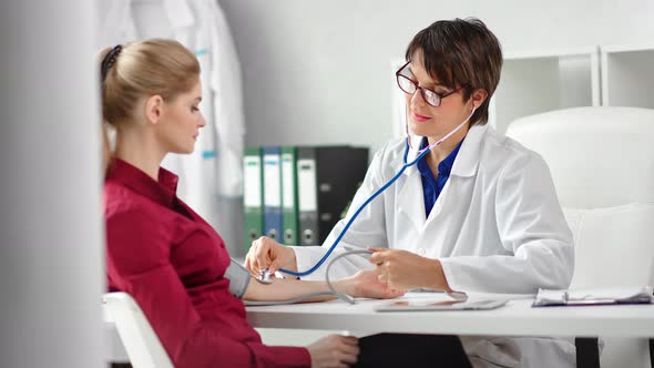 Positive Female Doctor Checking Pulse of Woman Patient Using Stethoscope Medical Equipment