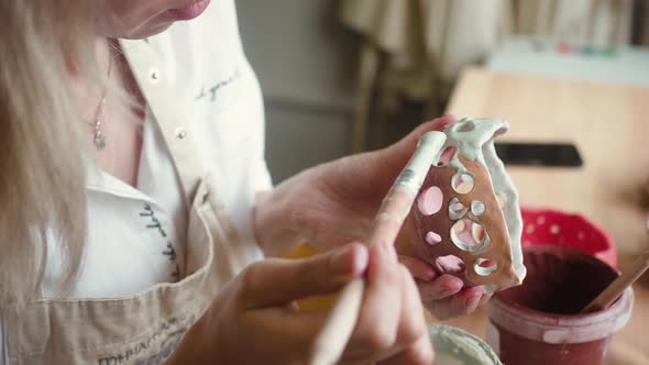 Close Up View of Female Potter Wearing Apron Using Glaze Brush to Paint on Pot