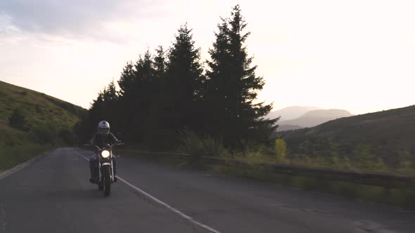 Man with Helm Riding Motorcycle on Country Road with Green Hills and Beautiful Sky