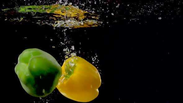 Vibrant bell peppers being dropped into water in slow motion.