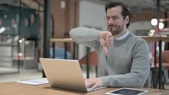 Young Man Showing Thumbs Down Sign While Using Laptop at Work