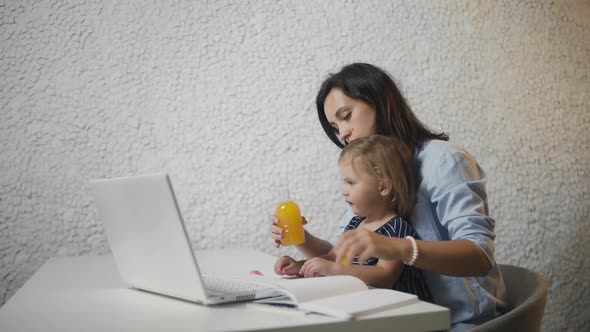 Young Mother Is Giving Juice To Her Baby From Bottle and Working on Notebook