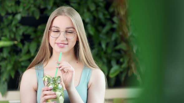 Portrait of Smiling Young Woman Posing with Fresh Detox Cocktail Sitting on Bench in Forest