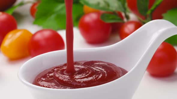 Pouring ketchup in bowl on white background with fresh tomatoes