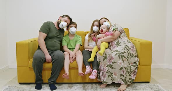 Family in Masks Sitting on Sofa. Overweight Mother and Father in Medical Masks Hugging Kids