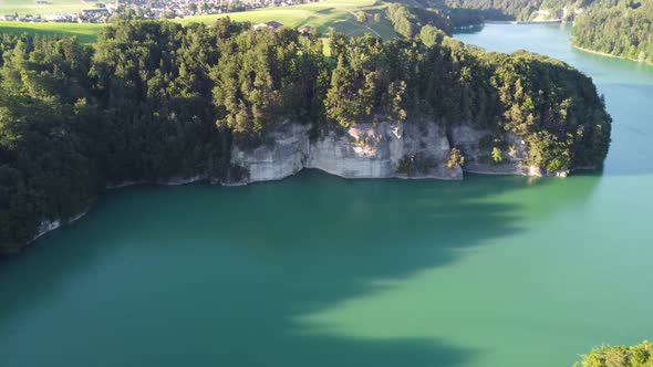 the evening sun casts long shadows over the Swiss lac de gruyere with an imposing rock in the foregr