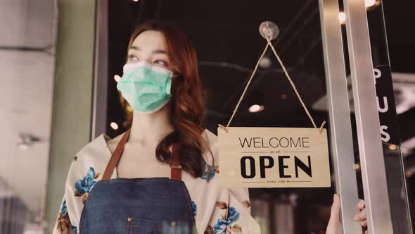 Business owner attractive young mixed race woman in apron hanging we're open sign
