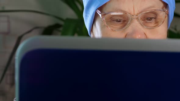 An Elderly Woman with Glasses Uses a Laptop