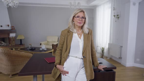 Blond Caucasian Woman in Eyeglasses Standing in Office at Table Looking at Camera Smiling