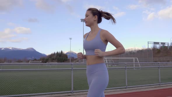 Mixed Race Asian Woman Jogging on Track, Slow Motion Profile Following