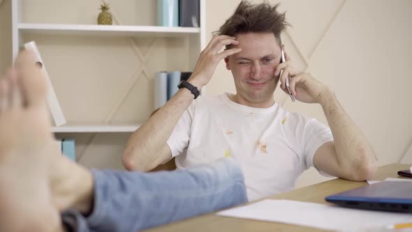 Portrait of Lazy Relaxed Man in Dirty T-shirt and Jeans Talking on the Phone and Laughing. Cheerful