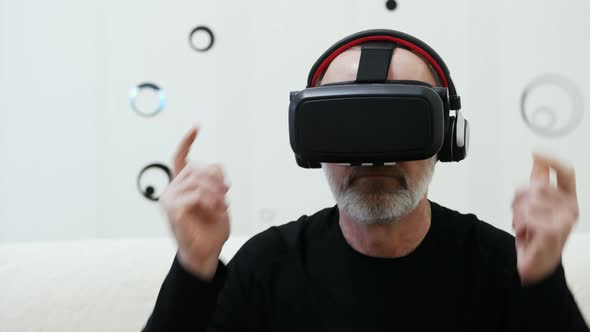 Modern Middle-aged Man with Grey Beard Puts on Wireless Headphones and Use VR Headset