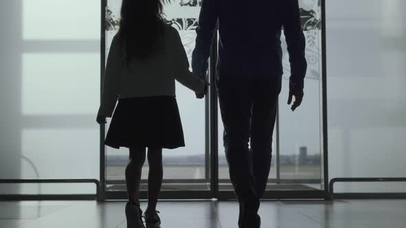 Silhouettes of Caucasian Man and Girl Walking Out the Airport Through Glass Door. Family Going To