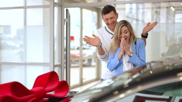 Loving Man Buying New Automobile for Woman in Car Dealership Surprising Partner