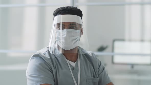 Male Doctor in Face Shield and Mask Posing for Camera at Work