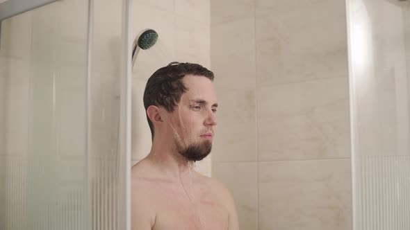 Portrait of Man Who Stands with a Serious View Under the Shower in the Bathroom