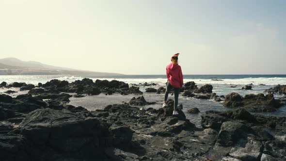 A Woman Walks Next to the Ocean Enjoying the Calm Scenery Against the Background of the Volcanic