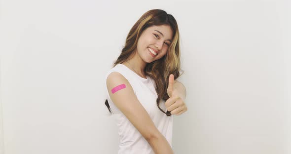 Asian Woman Shows Thumb Up And  Bandage On Arm. Happy Asian Woman Feels Good After Received Vaccine.