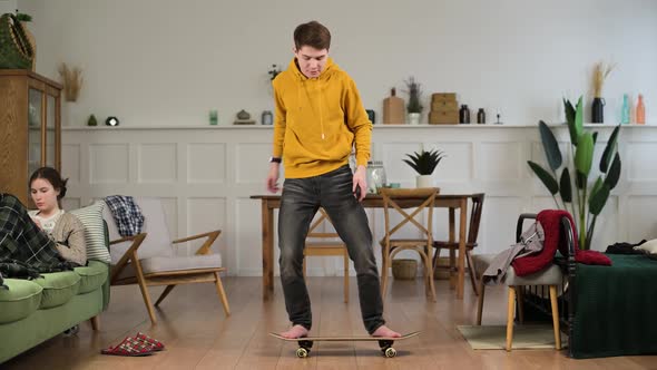 Young funny man at home learning to stand on a skateboard and falls